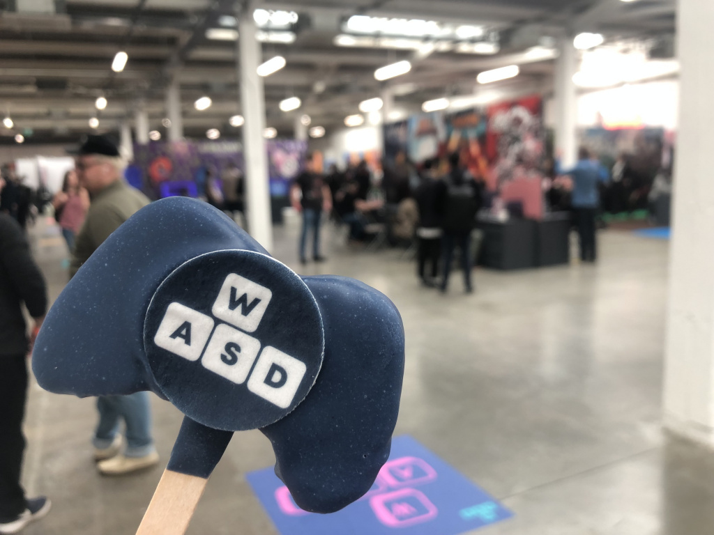 Publisher Collective at W.A.S.D. A blue controller shaped cookie with the letters W.A.S.D. printed on with a blurred background of the event.