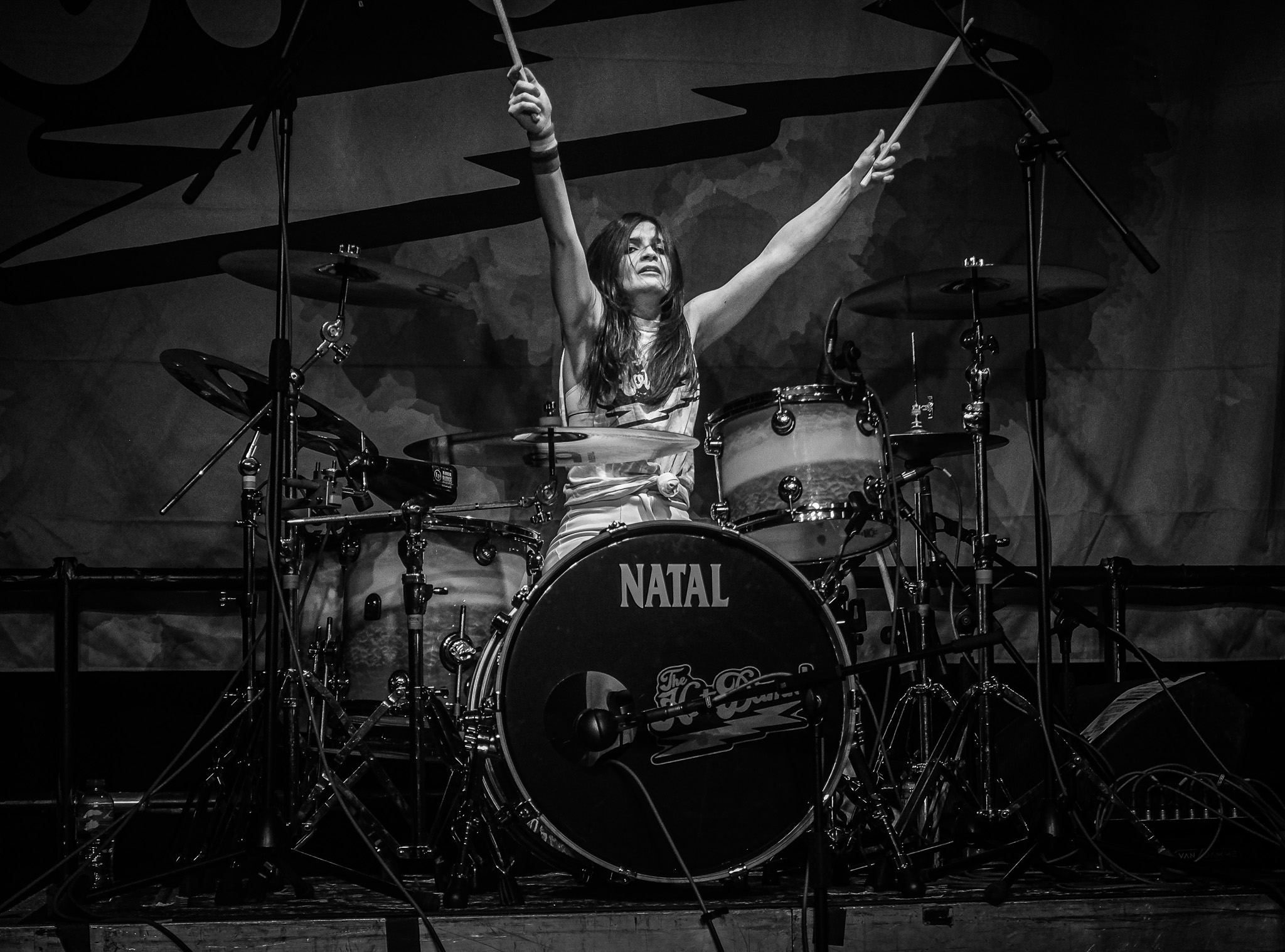 A female drummer with her arms raised in black and white